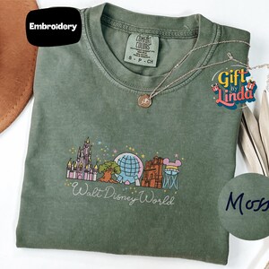 a green t-shirt with a Disney World logo, a necklace, and a hat, all placed on a white surface.