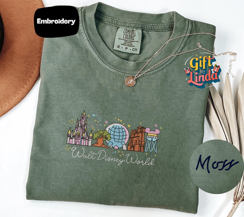 a green t-shirt with a Disney World logo, a necklace, and a hat, all placed on a white surface.