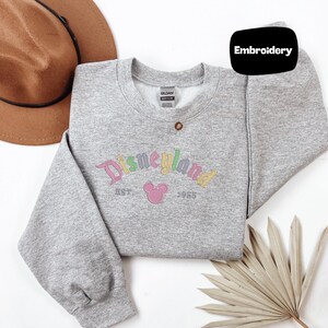 a gray sweatshirt with a Disney logo, a brown hat, and a palm frond, all arranged on a white background.