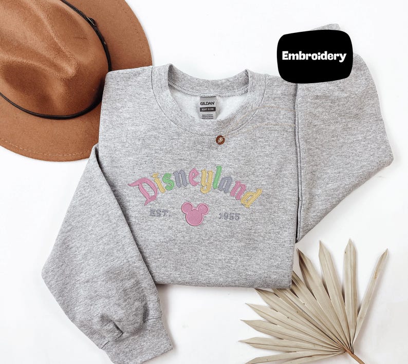 a gray sweatshirt with a Disney logo, a brown hat, and a palm frond, all arranged on a white background.