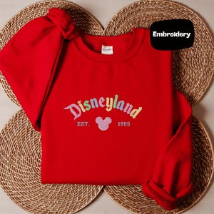 A red sweater with the text "Disneyland EST. 1955" and a Mickey Mouse logo, placed on a woven placemat.