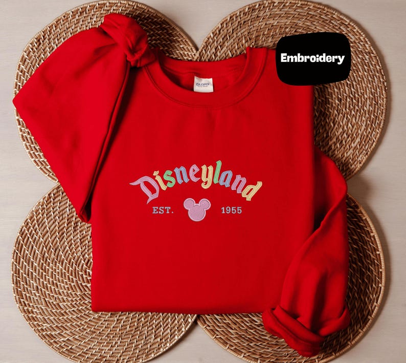 A red sweater with the text "Disneyland EST. 1955" and a Mickey Mouse logo, placed on a woven placemat.