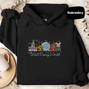 A black hoodie with a graphic design featuring various Disney landmarks and the text "Walt Disney World" printed on it.