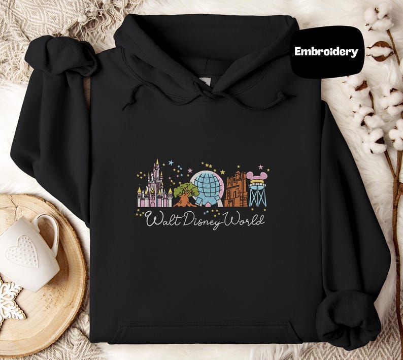 A black hoodie with a graphic design featuring various Disney landmarks and the text "Walt Disney World" printed on it.