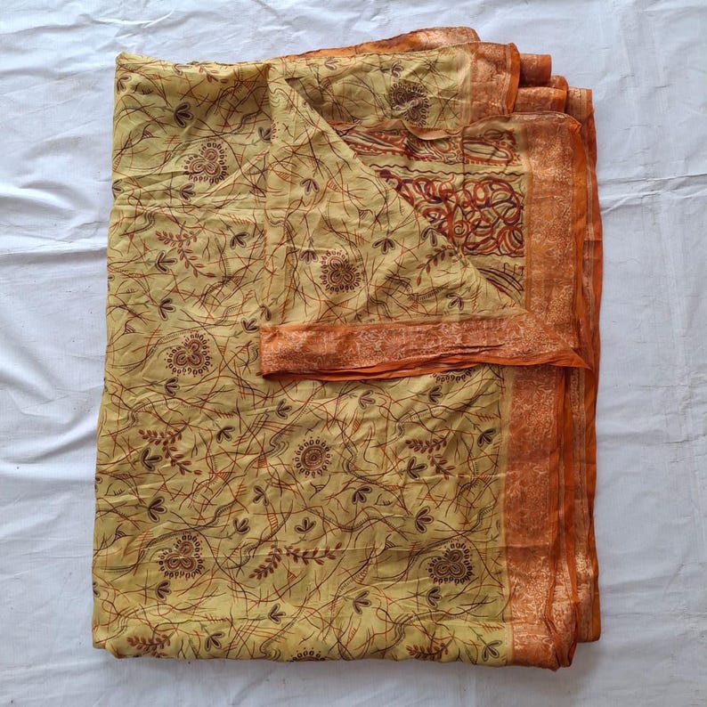 May include: A folded fabric textile featuring a light yellow base color with a dark brown linear pattern of thin, intersecting lines and small floral motifs. The edges are finished with a wide, solid orange border with a subtle texture.