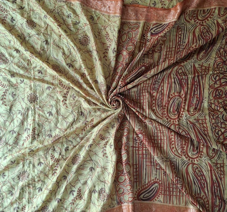May include: A fabric textile featuring a light yellow base with a complex pattern of dark brown and reddish-brown lines, swirling paisley shapes, and small circular motifs. The material is gathered in a central spiral, creating folds.