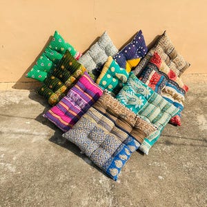May include: A collection of colorful, square floor cushions arranged in a heart shape. The cushions feature various patterns and colors, including green, pink, blue, and brown. Each cushion has a quilted design, adding texture and visual interest.