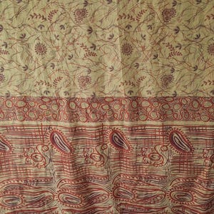 May include: A textile fabric featuring a cream-colored background with a dense pattern of thin, dark red and brown lines, small floral motifs, and circular shapes. A horizontal border displays repeating red paisley and abstract swirl designs.