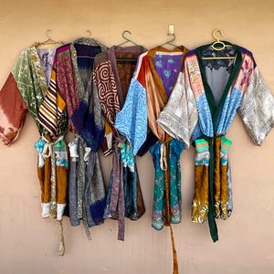 May include: Five open-front robes with long sleeves and matching waist ties, each featuring a unique patchwork of colorful, patterned fabrics including floral, geometric, and abstract designs in shades of green, brown, blue, purple, and gold.