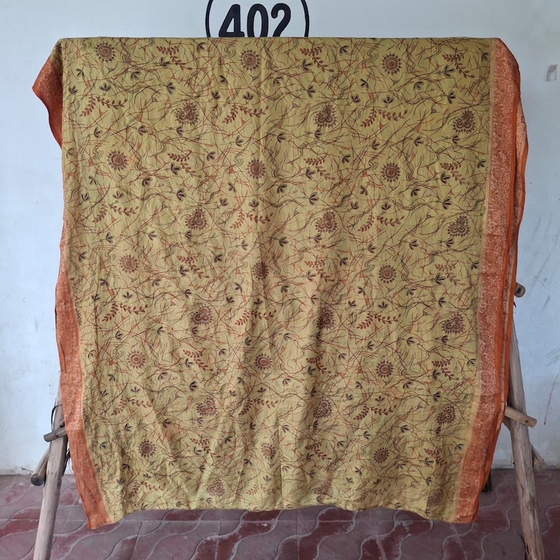 May include: A rectangular mustard yellow fabric featuring a dense, intricate pattern of dark brown swirling lines, small leaf motifs, and circular floral shapes. The fabric is framed by a wide, textured orange border with a detailed woven design.