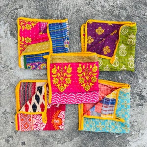 May include: Five colourful kantha quilts with yellow trim. The quilts are made of patchwork fabric and have a variety of floral and geometric patterns.