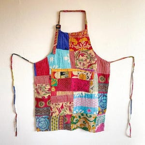 Peut inclure: Un tablier patchwork avec une variété de carrés de tissu colorés. Le tablier est doté d'une sangle de cou avec une boucle et de longues attaches. Les carrés de tissu comprennent des motifs floraux, rayés et à motifs dans des tons de rouge, bleu, rose et jaune.
