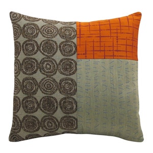 May include: A square throw pillow with a patchwork design. The pillow is made of three different fabrics: a brown fabric with a swirling pattern, a light gray fabric with a subtle texture, and an orange fabric with a grid pattern.