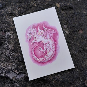 May include: A watercolor painting of a pink dragon with white markings. The dragon is curled up with its wings spread out. The background is a pink wash.