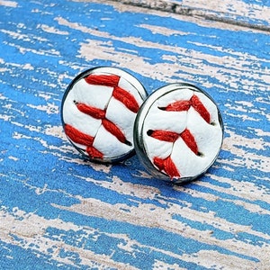 May include: A pair of silver baseball earrings with red stitching on a white background.