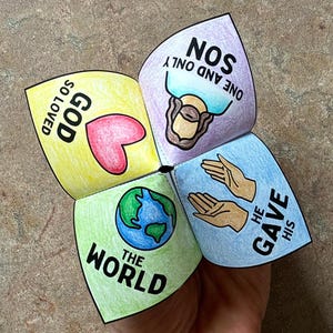 May include: A colorful paper fortune teller with hand-drawn illustrations and text. The fortune teller is open, revealing four sections with the phrases "GOD SO LOVED", "ONE AND ONLY SON", "HE GAVE HIS", and "THE WORLD".