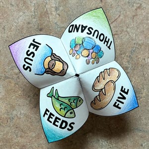 May include: A paper fortune teller game featuring hand-drawn illustrations and the text JESUS FEEDS FIVE THOUSAND. The four triangular flaps display a coloured drawing of Jesus, a group of people, two green fish, and two loaves of brown bread.