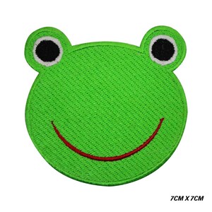 Könnte beinhalten: Ein grüner, gestickter Froschgesicht-Aufnäher mit schwarzen Augen und einem roten, lächelnden Mund. Der Aufnäher misst 7 cm x 7 cm.