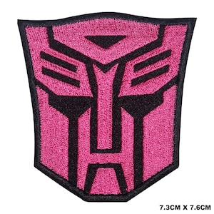 May include: Pink and black embroidered iron-on patch featuring a robot face with a geometric design. The patch measures 7.3 cm by 7.6 cm.