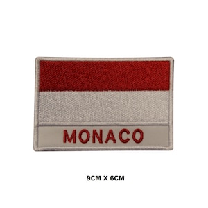 May include: Red and white embroidered patch with the word "MONACO" in red lettering. The patch is 9 cm by 6 cm.
