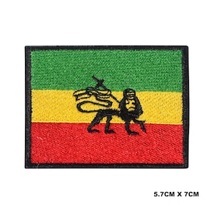 Pode incluir: Um remendo bordado com a bandeira rastafari nas cores verde, amarelo e vermelho. A bandeira tem um emblema de leão de Judá preto no centro.