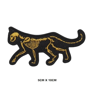 Könnte beinhalten: Schwarzer Bügel-Patch mit einem goldenen gestickten Skelett-Katzen-Design. Die Katze geht mit dem Kopf nach links gedreht. Der Patch misst 5 cm x 10 cm.