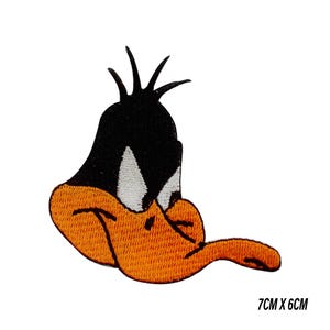 Puede incluir: Parche bordado con la cara de Daffy Duck, un personaje de dibujos animados. El parche es principalmente naranja, negro y blanco, con unas dimensiones de 7 cm x 6 cm. El diseño muestra el pico y la cabeza de Daffy Duck.