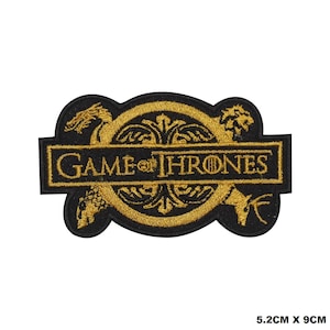 May include: A black and gold embroidered patch with the words "Game of Thrones" in a banner. The patch features a stylized design of a dragon, a wolf, and a lion.