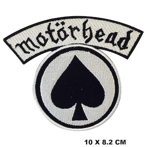 Puede incluir: Parche bordado blanco y negro con el texto "Motörhead" en una pancarta curva sobre una pica negra en un círculo blanco. El parche mide 10 x 8,2 cm.
