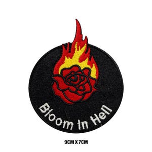 Op de afbeelding: Een geborduurde patch in zwart en wit met een rode roos in brand en de tekst "Bloom in Hell". De patch is 9 cm bij 7 cm.