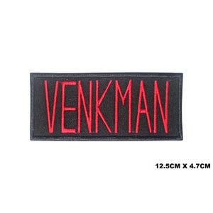 Może przedstawiać: Czarna naszywka haftowana z napisem "VENKMAN" w czerwonej nici. Naszywka ma wymiary 12,5 cm x 4,7 cm.