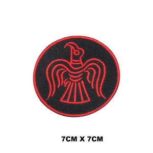 Könnte beinhalten: Roter gestickter Bügelaufkleber mit schwarzem Hintergrund. Der Patch zeigt einen stilisierten roten Vogel mit ausgebreiteten Flügeln. Der Patch ist 7 cm x 7 cm groß.