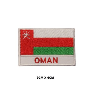 Pode incluir: Um remendo bordado com a bandeira de Omã. A bandeira é vermelha, branca e verde com um símbolo branco no canto superior esquerdo. O remendo mede 9 cm por 6 cm e tem a palavra "OMÃ" escrita abaixo da bandeira.