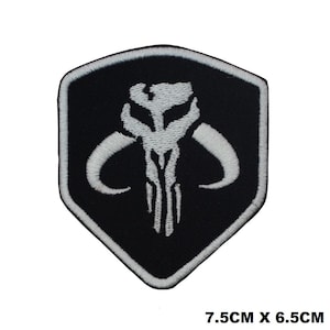 May include: Black and white embroidered patch featuring a Mandalorian symbol. The symbol is a white skull with horns and a white design on a black shield. The patch measures 7.5cm by 6.5cm.