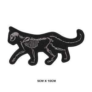 Pode incluir: Patch bordado preto em forma de gato, com um design de esqueleto. Mede 5 cm x 10 cm. O gato é retratado em movimento, com o esqueleto visível em fio cinza. Artigo decorativo.