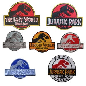 Può includere: Una collezione di sette toppe ricamate con vari loghi di Jurassic Park e Jurassic World. I disegni includono sagome di dinosauri in rosso, nero, arancione, argento, blu e bianco, con testi come The Lost World, Fallen Kingdom e Ranger.