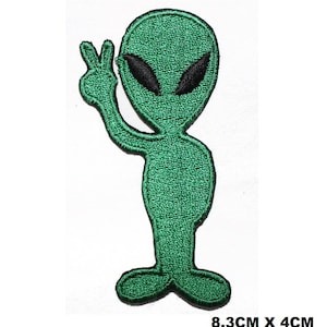 以下が含まれることがあります： 黒い目をした緑色の宇宙人の刺繍パッチで、ピースサインをしています。パッチのサイズは8.3cm x 4cmです。