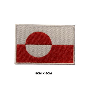 May include: A white and red embroidered patch of the flag of Greenland. The flag features a red disc with a white crescent on a white background. The patch is 9 cm by 6 cm.