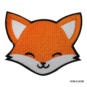 Pode incluir: Patch bordado com o rosto sorridente de uma raposa. A raposa tem pelo laranja, detalhes brancos nas orelhas e rosto, e contorno preto. Mede 7 cm x 6 cm.