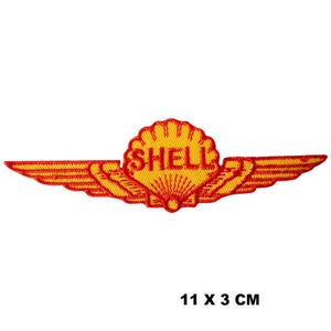 Puede incluir: Parche bordado rojo y amarillo con el logotipo de Shell y alas. El logotipo es una concha amarilla con la palabra "SHELL" en letras rojas. Las alas son rojas con detalles amarillos. El parche mide 11 cm por 3 cm.