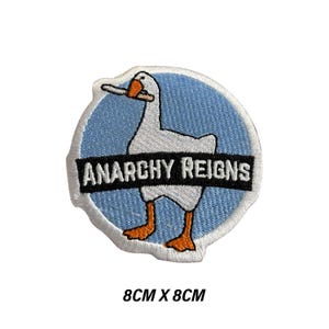 Op de afbeelding: Geborduurde patch met een witte gans, oranje snavel en poten, op een lichtblauwe achtergrond. De tekst "ANARCHY REIGNS" staat op een zwarte banner. De patch meet 8 cm x 8 cm.