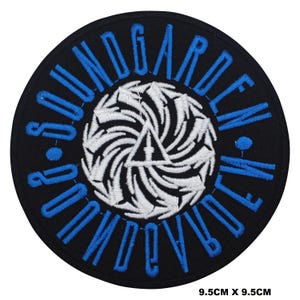 May include: A black and blue embroidered patch with the words "SOUNDGARDEN" in a circle. The centre of the patch features a white and black swirling design.