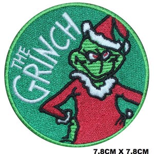 Op de afbeelding: Groene geborduurde patch met de Grinch die een rood-witte kerstmanpak draagt met de tekst "The Grinch" in wit.