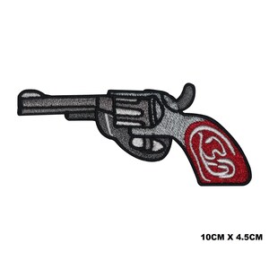 Könnte beinhalten: Ein gestickter Bügeleisen-Aufnäher mit einem Revolver mit rotem Griff. Der Aufnäher ist 4,5 cm x 10 cm groß.