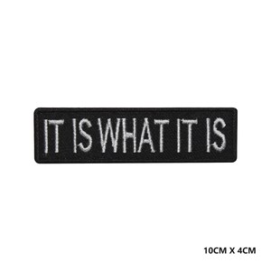 May include: Black embroidered patch with white text that reads "IT IS WHAT IT IS". The patch is 4 cm wide and 10 cm long.