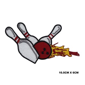 Könnte beinhalten: Ein gestickter Bügelaufkleber mit einem roten Bowlingball mit drei Löchern und zwei weißen Bowlingkegeln mit roten Streifen. Der Bowlingball steht in Flammen mit gelben Flammen.