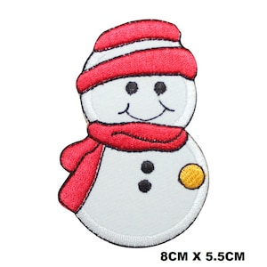 May include: A white snowman with a red hat and scarf. The snowman has a black button nose and two black eyes. The snowman is holding a yellow circle in its right hand. The snowman is 8 cm wide and 5.5 cm tall.