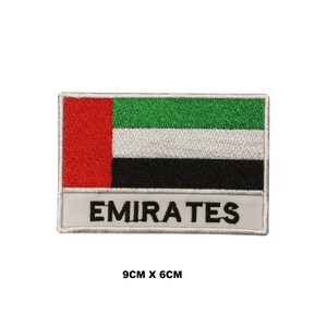 Pode incluir: Um remendo bordado com a bandeira dos Emirados Árabes Unidos com a palavra "EMIRATES" abaixo. O remendo é branco com uma bandeira vermelha, verde, branca e preta no centro. O remendo mede 9 cm por 6 cm.