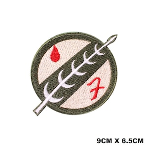 Può includere: Toppa ricamata verde e bianca con una goccia di sangue rossa e una pianta stilizzata bianca. La toppa ha un "7" rosso al centro e misura 9 cm per 6,5 cm.