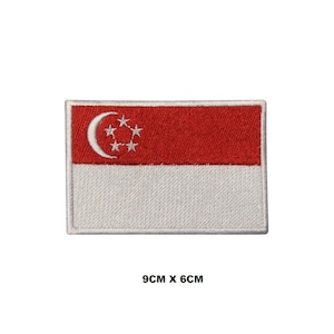 Puede incluir: Un parche bordado con la bandera de Singapur. La bandera es roja y blanca con una luna creciente y cinco estrellas en la esquina superior izquierda. El parche mide 9 cm por 6 cm.
